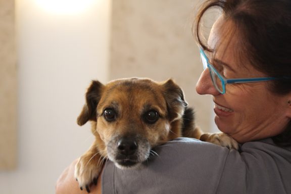 Frau mit Brille hält einen Hund auf dem Arm und lächelt.