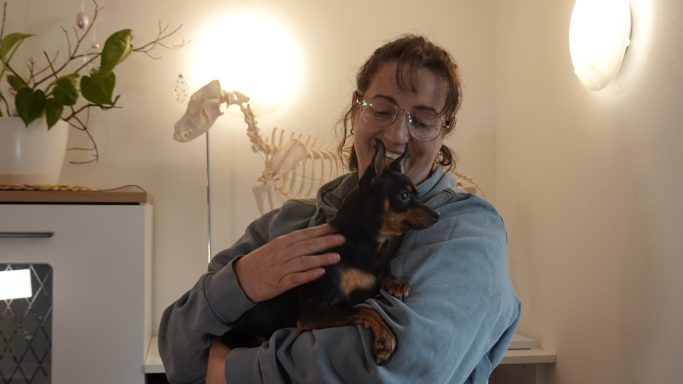 Person mit Hund in der Küche, lächelt und hält den Hund in den Armen.